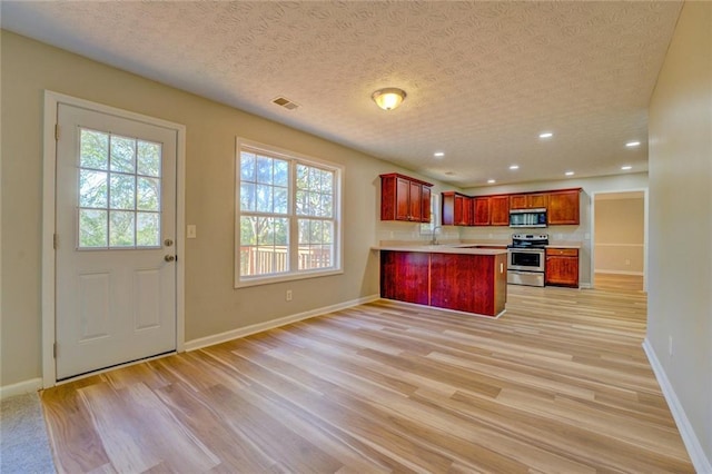 kitchen with kitchen peninsula, appliances with stainless steel finishes, a textured ceiling, and light hardwood / wood-style flooring