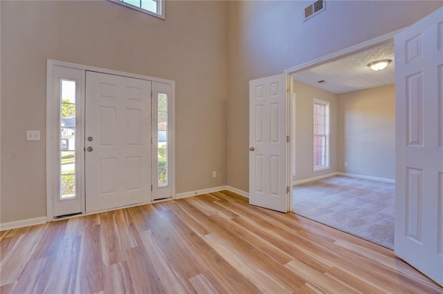 foyer entrance featuring a towering ceiling, a healthy amount of sunlight, and light wood-type flooring