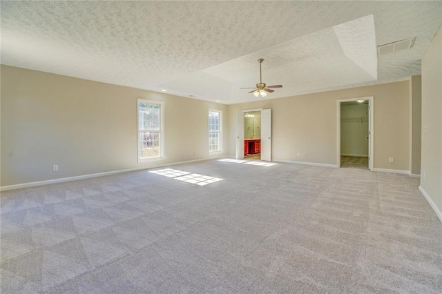 empty room with ceiling fan, a raised ceiling, light colored carpet, and a textured ceiling