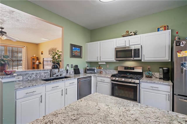 kitchen with white cabinets, a ceiling fan, appliances with stainless steel finishes, a peninsula, and a sink