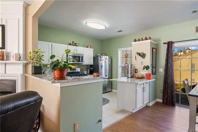 kitchen featuring a peninsula, light stone countertops, appliances with stainless steel finishes, and white cabinets