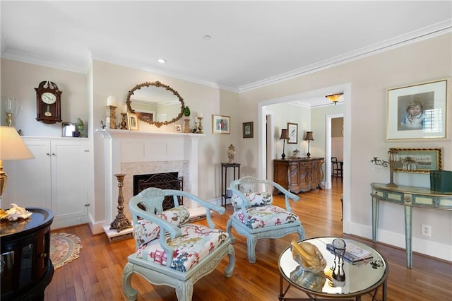 living room with a fireplace with raised hearth, ornamental molding, wood finished floors, and baseboards