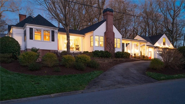 view of front facade featuring driveway, a chimney, and a front yard