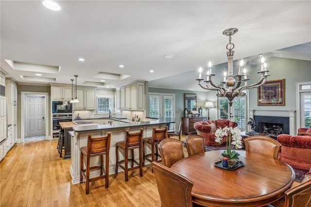 dining area featuring ornamental molding, a raised ceiling, light wood-type flooring, and a notable chandelier