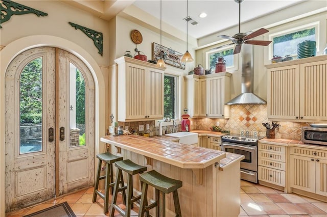 kitchen featuring stainless steel appliances, sink, wall chimney exhaust hood, tile counters, and backsplash