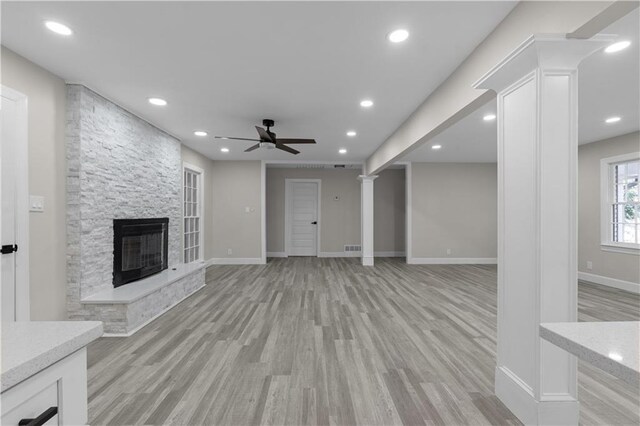 unfurnished living room featuring decorative columns, a stone fireplace, ceiling fan, and light wood-type flooring