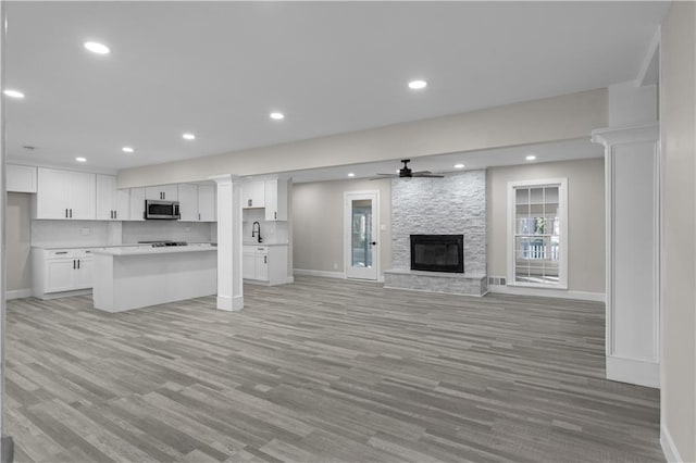 unfurnished living room with ceiling fan, light hardwood / wood-style floors, and a stone fireplace