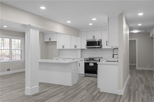 kitchen with kitchen peninsula, appliances with stainless steel finishes, light wood-type flooring, sink, and white cabinets