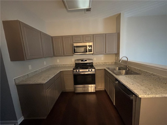 kitchen with gray cabinetry, dark wood-type flooring, sink, light stone countertops, and stainless steel appliances