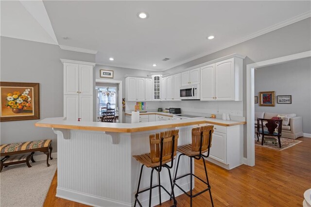 kitchen featuring white microwave, a breakfast bar area, light countertops, light wood-style flooring, and white cabinetry