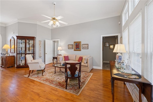 living area featuring light wood finished floors, baseboards, crown molding, and a towering ceiling