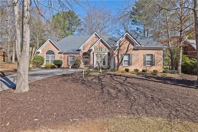 ranch-style house with concrete driveway, brick siding, and roof with shingles