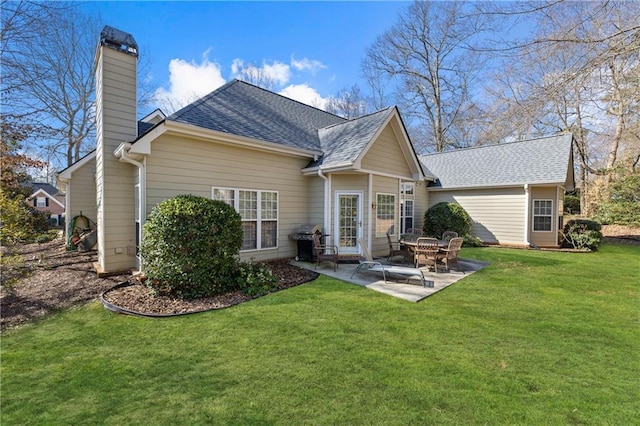 back of property featuring a yard, roof with shingles, a chimney, and a patio area