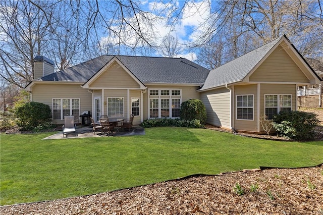 rear view of property featuring a lawn, a chimney, a patio, and roof with shingles