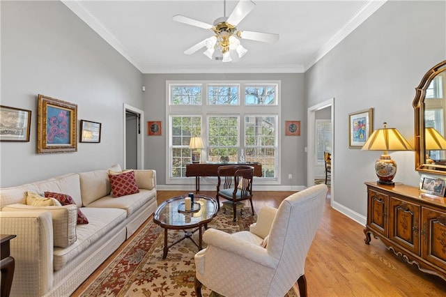 living room with a ceiling fan, baseboards, a high ceiling, light wood-style flooring, and ornamental molding