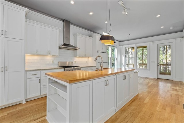 kitchen featuring white cabinets, wall chimney exhaust hood, stainless steel range oven, and an island with sink