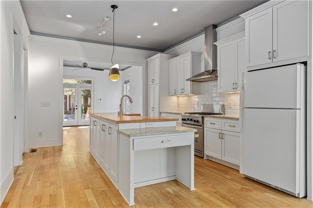 kitchen with white cabinetry, stainless steel range, wall chimney exhaust hood, white refrigerator, and a center island with sink