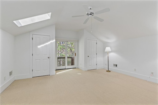 additional living space with light colored carpet, ceiling fan, and vaulted ceiling with skylight