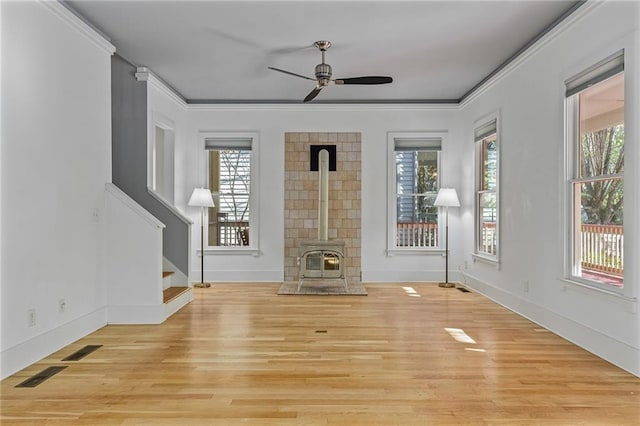 interior space featuring ceiling fan, a wood stove, crown molding, and light hardwood / wood-style flooring