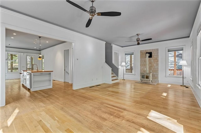 unfurnished living room featuring ceiling fan, light wood-type flooring, a wood stove, and a wealth of natural light