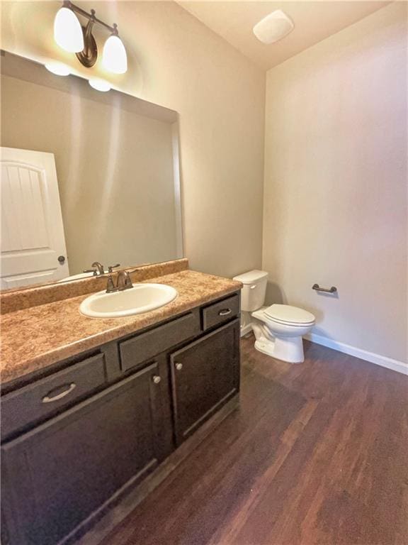 bathroom with vanity, toilet, wood finished floors, and baseboards