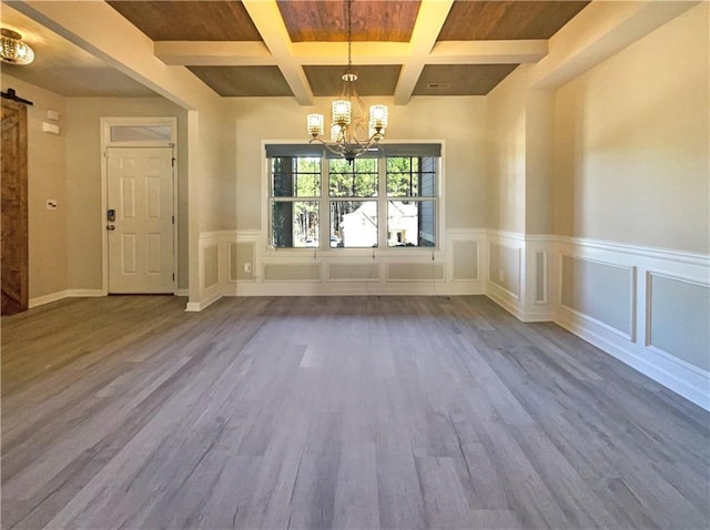 unfurnished dining area featuring wood finished floors, coffered ceiling, an inviting chandelier, beam ceiling, and a barn door