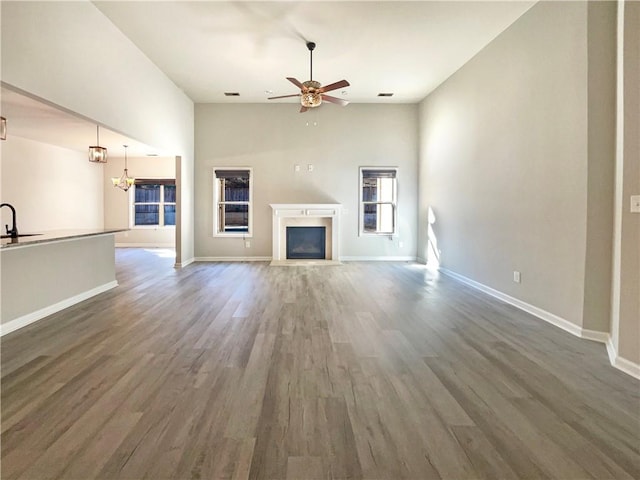 unfurnished living room featuring ceiling fan with notable chandelier, a sink, wood finished floors, a fireplace, and baseboards