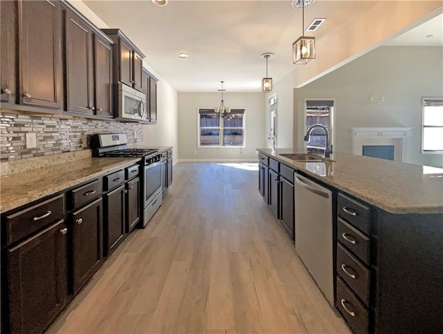 kitchen with an inviting chandelier, a sink, appliances with stainless steel finishes, light wood-type flooring, and backsplash