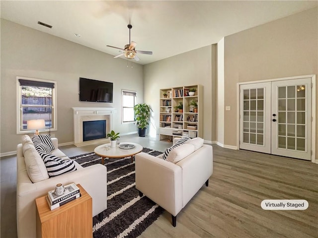 living area featuring wood finished floors, baseboards, visible vents, ceiling fan, and a glass covered fireplace