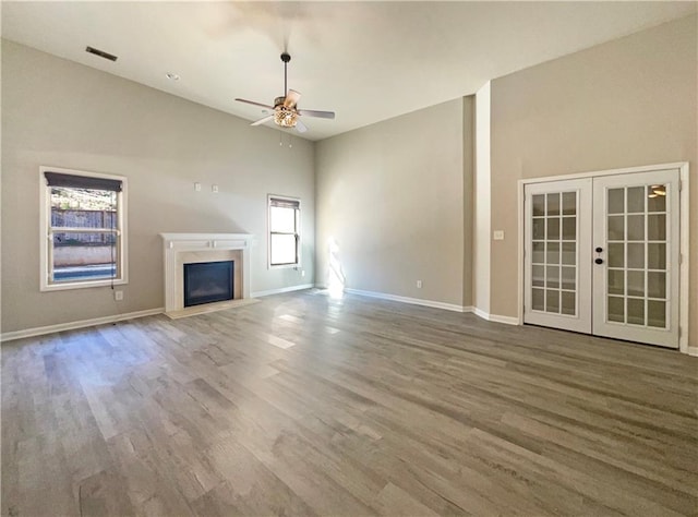 unfurnished living room with a fireplace with raised hearth, french doors, ceiling fan, and wood finished floors
