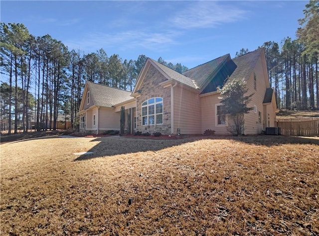 view of home's exterior featuring stone siding, cooling unit, and a shingled roof