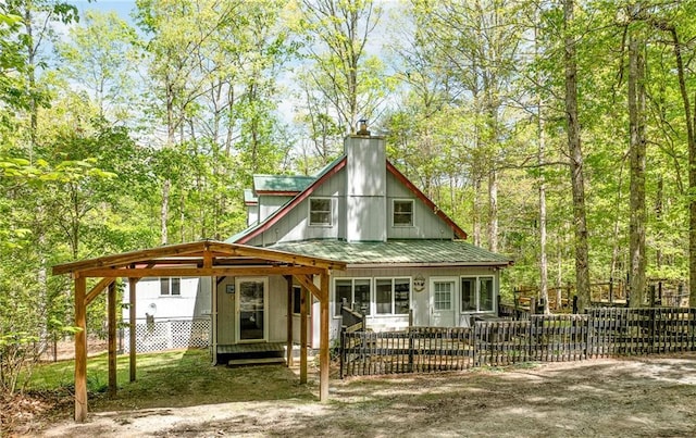 back of house featuring a chimney, metal roof, and a fenced front yard
