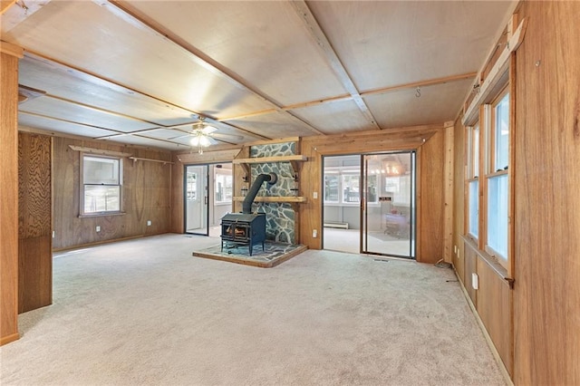 interior space with a wood stove, carpet flooring, wood walls, and plenty of natural light