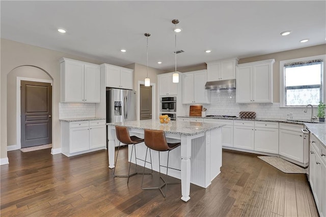 13015 Fox Rd, Alpharetta, GA 30005 - kitchen featuring under cabinet range hood, appliances with stainless steel finishes, backsplash, white cabinetry, and a center island