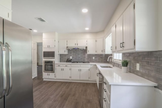kitchen featuring stainless steel appliances, a sink, dark wood-type flooring, light countertops, and white cabinetry