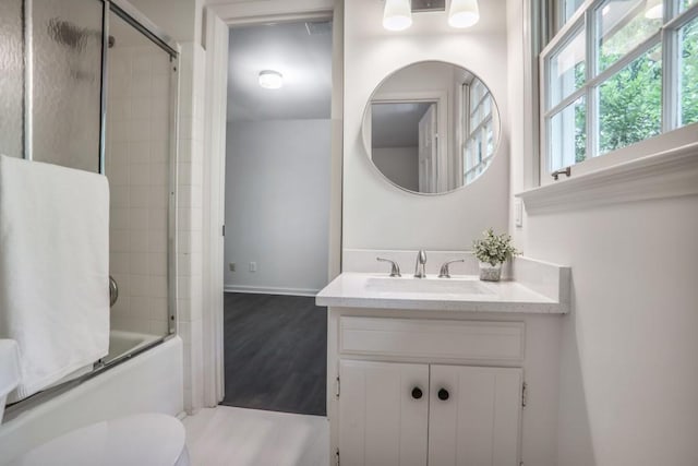 bathroom featuring shower / bath combination with glass door, vanity, toilet, baseboards, and wood finished floors