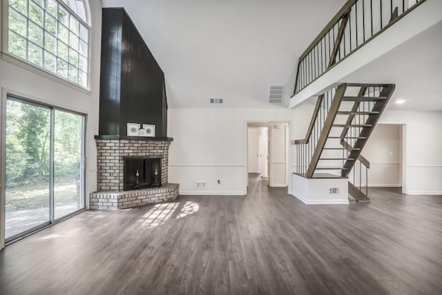 unfurnished living room with a towering ceiling, stairs, baseboards, dark wood finished floors, and plenty of natural light