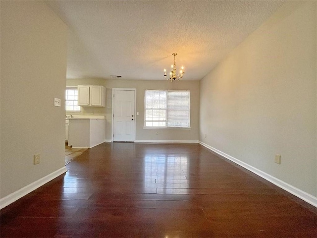 unfurnished living room with a notable chandelier, a textured ceiling, and hardwood / wood-style flooring