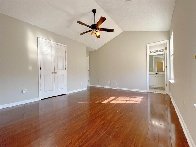 interior space with lofted ceiling, a textured ceiling, connected bathroom, ceiling fan, and hardwood / wood-style floors