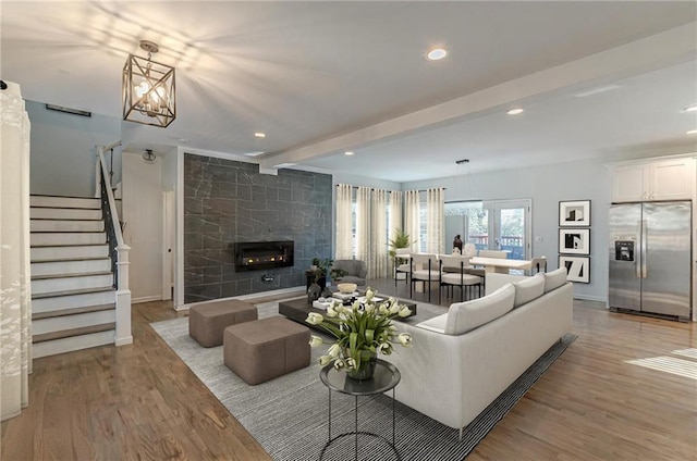 living room featuring a tiled fireplace, light hardwood / wood-style floors, a notable chandelier, and beamed ceiling