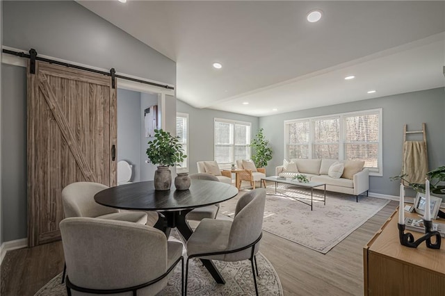 dining area with vaulted ceiling, a barn door, and light wood-type flooring