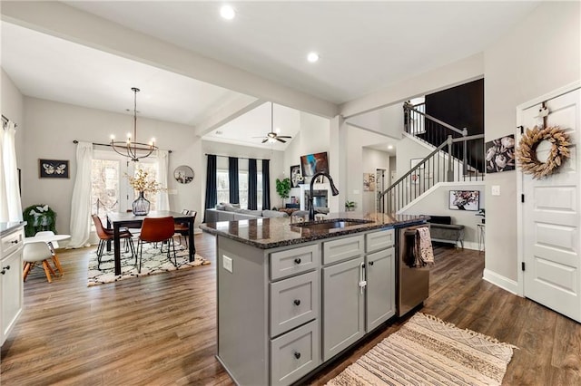 kitchen featuring dark wood-style flooring, stainless steel dishwasher, open floor plan, a sink, and dark stone counters