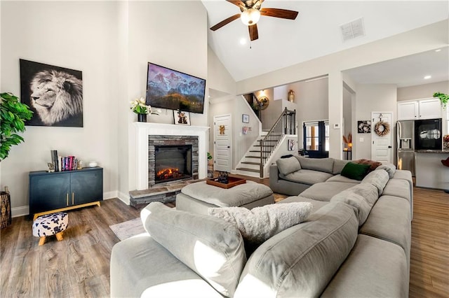 living room featuring visible vents, a stone fireplace, wood finished floors, high vaulted ceiling, and stairs