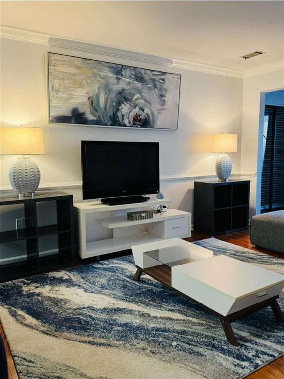 living area with visible vents, crown molding, and wood finished floors