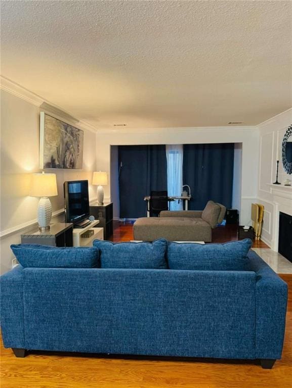 living area with a fireplace with flush hearth, a textured ceiling, wood finished floors, and crown molding