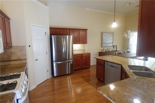 kitchen with sink, dark wood-type flooring, stainless steel appliances, ornamental molding, and decorative light fixtures