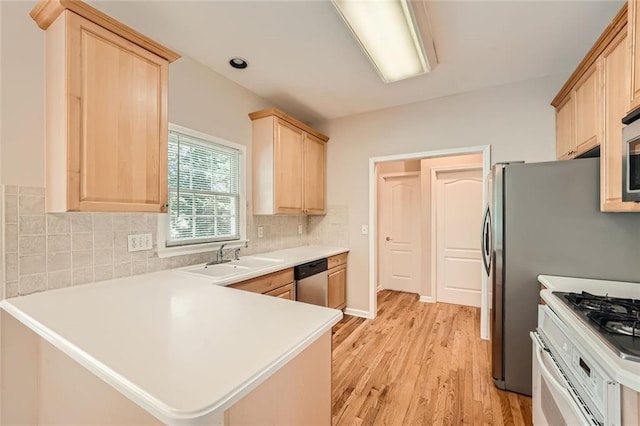 kitchen with appliances with stainless steel finishes, sink, decorative backsplash, kitchen peninsula, and light hardwood / wood-style flooring