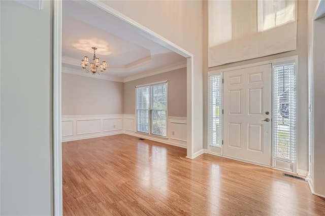 foyer with ornamental molding, light hardwood / wood-style flooring, a notable chandelier, and a tray ceiling