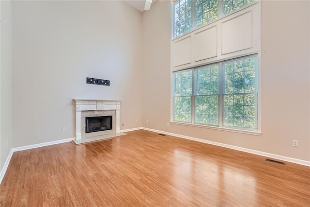 unfurnished living room with a fireplace, light hardwood / wood-style floors, and a high ceiling