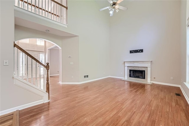 unfurnished living room with a towering ceiling, light hardwood / wood-style floors, a premium fireplace, and ceiling fan